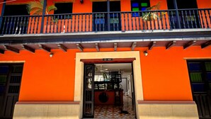 A two-story building with a vibrant orange facade, a balcony with black railings, and a tiled entrance. - Hotel Puerto Pelicano (Santa Marta)