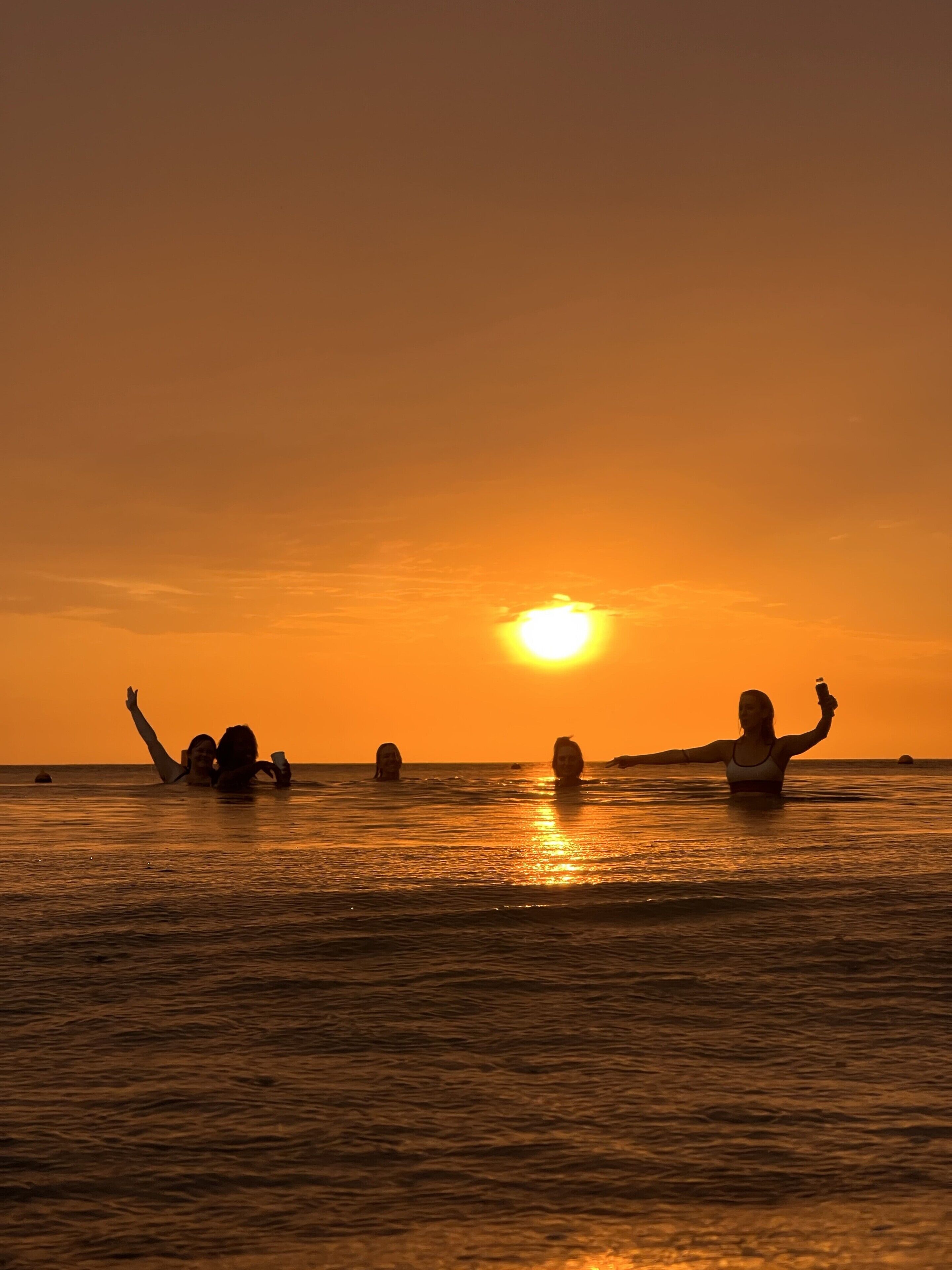 Atardecer sobre el océano con siluetas de personas en el agua.