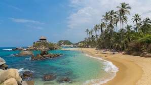 A beach with clear turquoise water, a sandy shore, and palm trees. - Hotel Puerto Pelicano (Santa Marta)