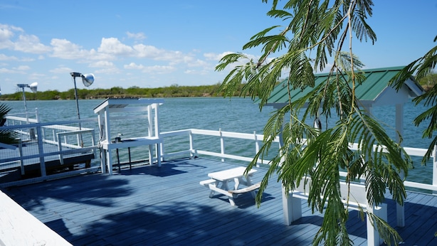 Een houten terras met picknicktafels en een overdekte zithoek met uitzicht op een waterpartij.