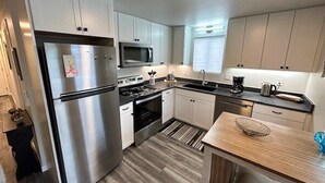 Una cocina moderna con electrodomésticos de acero inoxidable, armarios blancos y encimera de madera.
