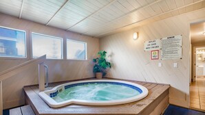 Un jacuzzi en una habitación con paredes y techo de madera, una planta en maceta y un cartel con normas del spa.