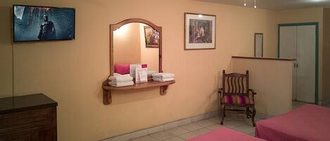 A hotel room with two beds, a wooden dresser, a chair, a ceiling fan, a wall-mounted TV, and a framed picture.