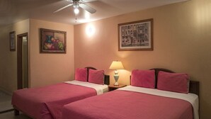 Habitación de hotel con dos camas, cada una con ropa de cama rosa, una mesita de noche con lámpara y un ventilador de techo.