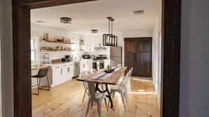 Cozinha moderna com armários brancos, uma mesa de jantar de madeira e uma porta de madeira escura.