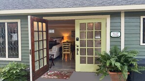 A cottage with a green exterior, a wooden door with glass panels, a bed, a chair, and a sign indicating it's a carriage house cottage. - Tiny House Cottage in Historic Downtown (Little Rock)