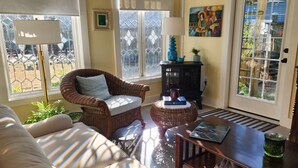 A cozy living room with a wicker armchair, a wooden coffee table, and a sofa. There is a fireplace, a lamp, and a window with a view of the outside. - Tiny House Cottage in Historic Downtown (Little Rock)