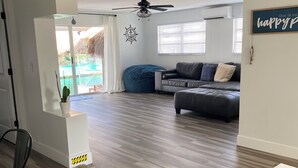 Un'ampia zona giorno con un divano grigio, un pouf blu e una ventola a soffitto.