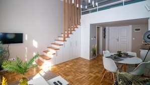 A modern living room with a wooden staircase, a dining area, and a flat-screen TV mounted on the wall. - Palms Apartments Budapest (Budapest)