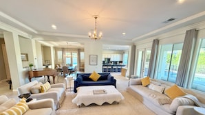 A spacious living room with a chandelier, sofas, a piano, and a view of the kitchen and outdoor area. - 1/2acre Adult & Kid Playground-relax & have fun! Pool/spa-golf-tennis-shopping (La Quinta)