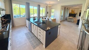 A modern kitchen with a central island, large windows, and a dining area with a fireplace. - 1/2acre Adult & Kid Playground-relax & have fun! Pool/spa-golf-tennis-shopping (La Quinta)