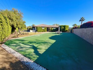 Un barrio residencial con césped verde, un patio con mobiliario exterior y una casa con tejado de tejas.