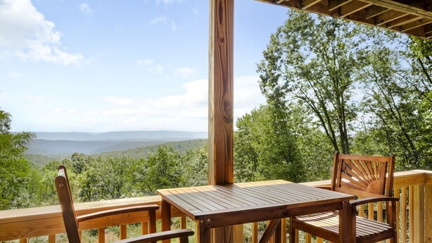 Una terraza de madera con una mesa y sillas, con vista a un paisaje montañoso.