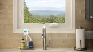 Una cocina con ventana que da a un paisaje montañoso, un lavabo de acero inoxidable y un dispensador de jabón.