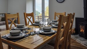 A dining area with a wooden table set for four, chairs, a clock, and a fireplace.