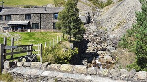 A stone building with a stone facade, a wooden fence, and a rocky landscape with a waterfall.