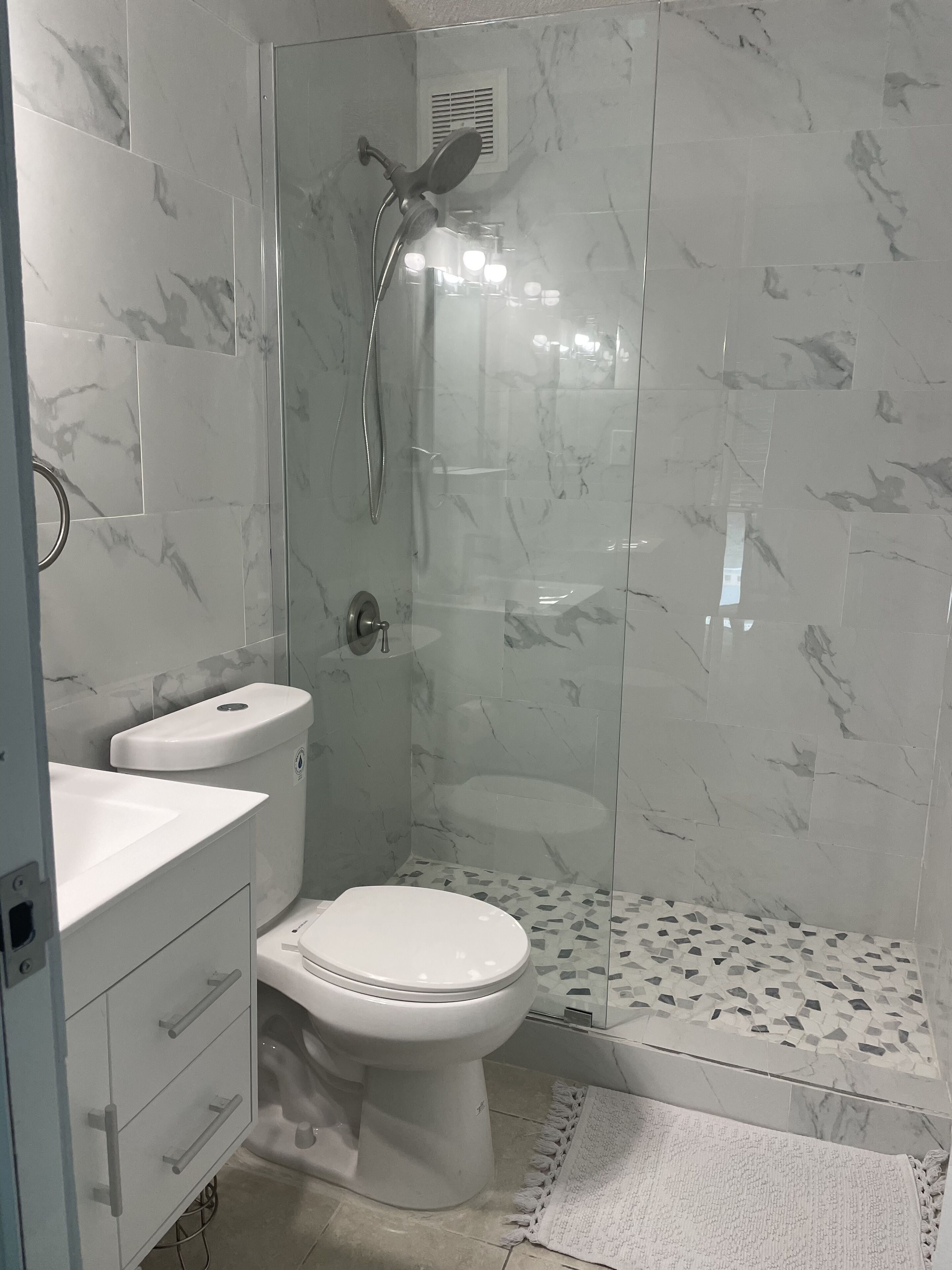 A modern bathroom with a glass-enclosed shower, a white toilet, and a marble-tiled wall.