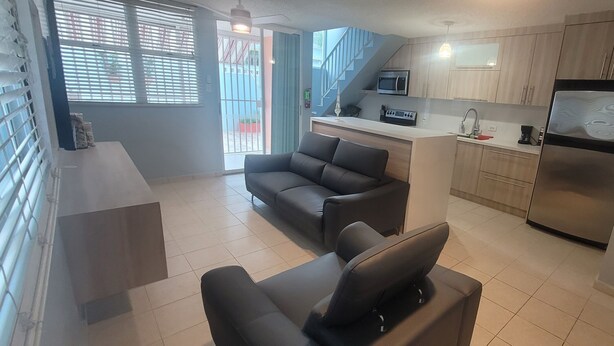 A modern kitchen with a built-in microwave, a refrigerator, and a sink. There is a seating area with a sofa and a chair. - Walk to beach & Kioskos, close to rainforest, cold air, free parking  (Luquillo)