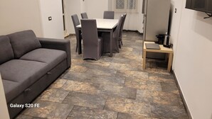 A compact living space with a grey sofa, a dining table with chairs, a small wooden table with a kettle, and a TV on the wall. - 5 minutes walk from saint peter vatican museums castel sant angelo. At 50m meter (Roma)