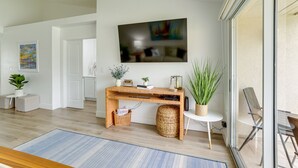 Ein modernes Wohnzimmer mit Schreibtisch aus Holz, einem Flachbildfernseher und einer gemütlichen Sitzecke mit Sessel und Hocker.
