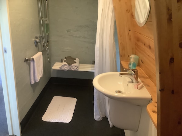 A bathroom with a white sink, a shower, a towel rack, and a small shelf with toiletries.