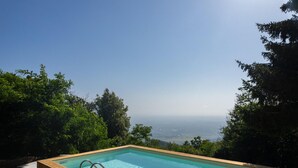A rectangular pool with a wooden deck and metal handrails, surrounded by lush greenery and overlooking a distant landscape. - Lovely home in Calci (PI) (Calci (PI))