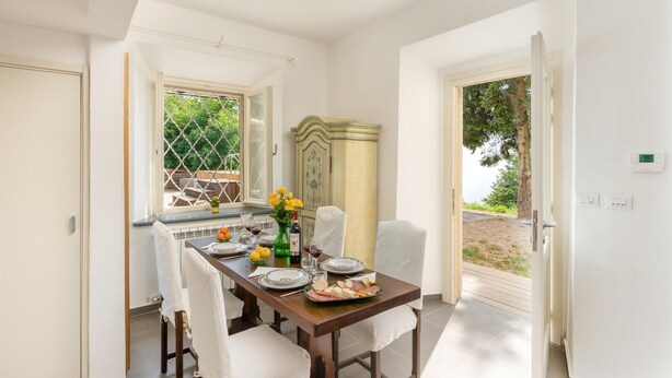 A dining area with a wooden table set for four, a vintage cabinet, and a view of the outdoors through a window. - Lovely home in Calci (PI) (Calci (PI))