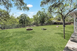 A well-maintained grassy yard with a fire pit, a bench, and a fenced area.