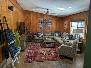 Uma sala de estar aconchegante com parede de madeira, ventilador de teto, mesa de centro e sofá.