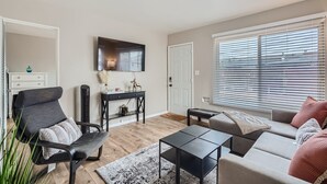 A modern living room with a grey sofa, a black armchair, a coffee table, and a TV mounted on the wall. - OB Cottage w outdoor patio / 3 min to the beach   (San Diego)
