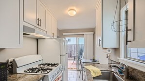 A modern kitchen with white cabinets, a gas stove, stainless steel sink, and a window overlooking a backyard. - OB Cottage w outdoor patio / 3 min to the beach   (San Diego)
