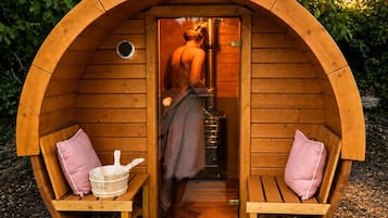 A wooden sauna with a bench and a bench seat, a towel, a bucket, and a mat.