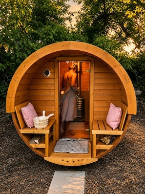 A wooden sauna with a bench and a bench seat, a towel, a bucket, and a mat.
