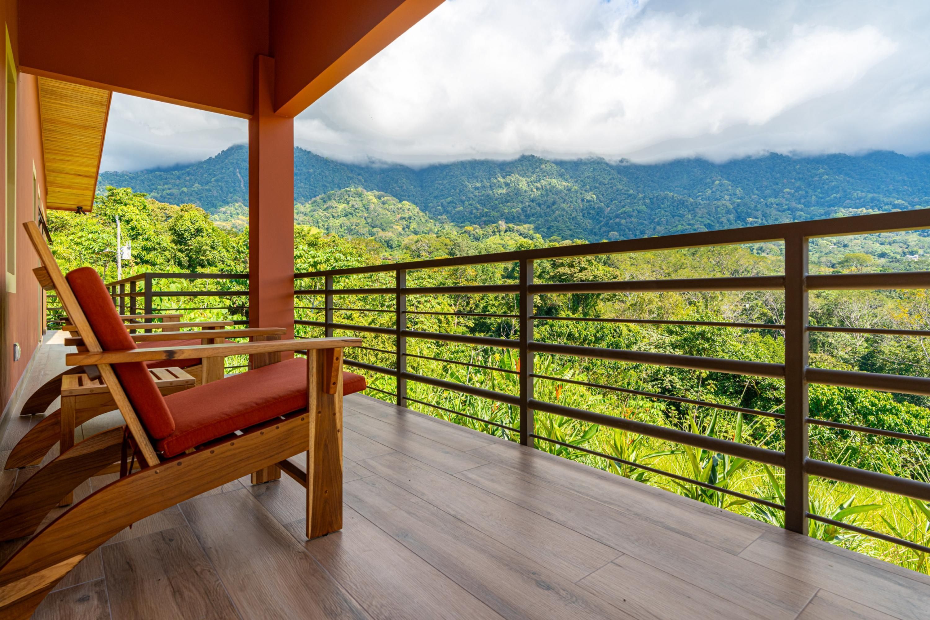 A balcony with a wooden floor, a red cushioned chair, and a view of a mountainous landscape.