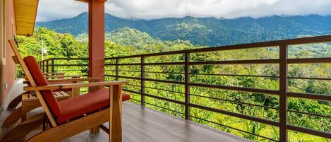 A balcony with a wooden floor, a red cushioned chair, and a view of a mountainous landscape.