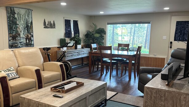 A spacious living room with a leather sofa, a coffee table, and a dining area with wooden chairs and a table. - Montana Forest Retreat, Easy Walk to Flathead Lake, 1.5 Acres Fenced for Dogs! (Polson)