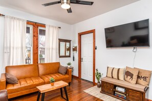 A living room with a leather sofa, a wooden coffee table, a TV mounted on the wall, and a door with a mirror. - Three bedroom apartment in Buffalo & Niagara region 🌊 (Buffalo)