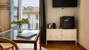 Ein Zimmer mit einem Glastisch, einer weißen Kommode mit Fernseher und Blick auf Gebäude durch ein Fenster.