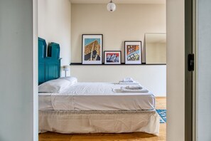 A hotel room with a bed, a teal-colored wardrobe, and framed pictures on the wall.