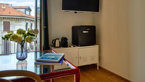Ein Zimmer mit Fernseher, Minibar, Blumen in einer Vase und einem Buch auf einem Glastisch.