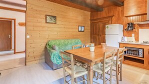 Un accogliente interno di una baita con un tavolo da pranzo in legno, sedie, un divano con una coperta verde, un angolo cottura con frigorifero, macchina del caffè e tostapane.