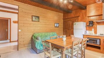 L’intérieur chaleureux d’un chalet avec une table à manger en bois, des chaises, un canapé recouvert d’une couverture verte, un coin cuisine équipé d’un réfrigérateur, d’une machine à café et d’un grille-pain.