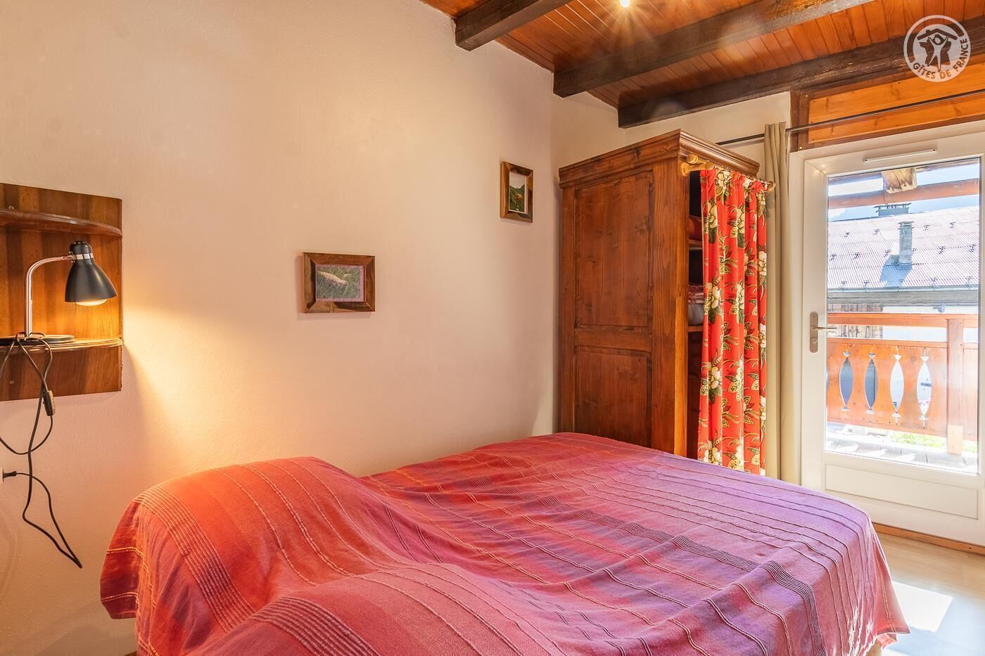 Une chambre à coucher avec un lit, une armoire en bois, une lampe de bureau et une fenêtre avec des rideaux.