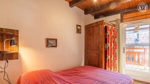 Una camera da letto con un letto, un armadio in legno, una lampada da scrivania e una finestra con tende.