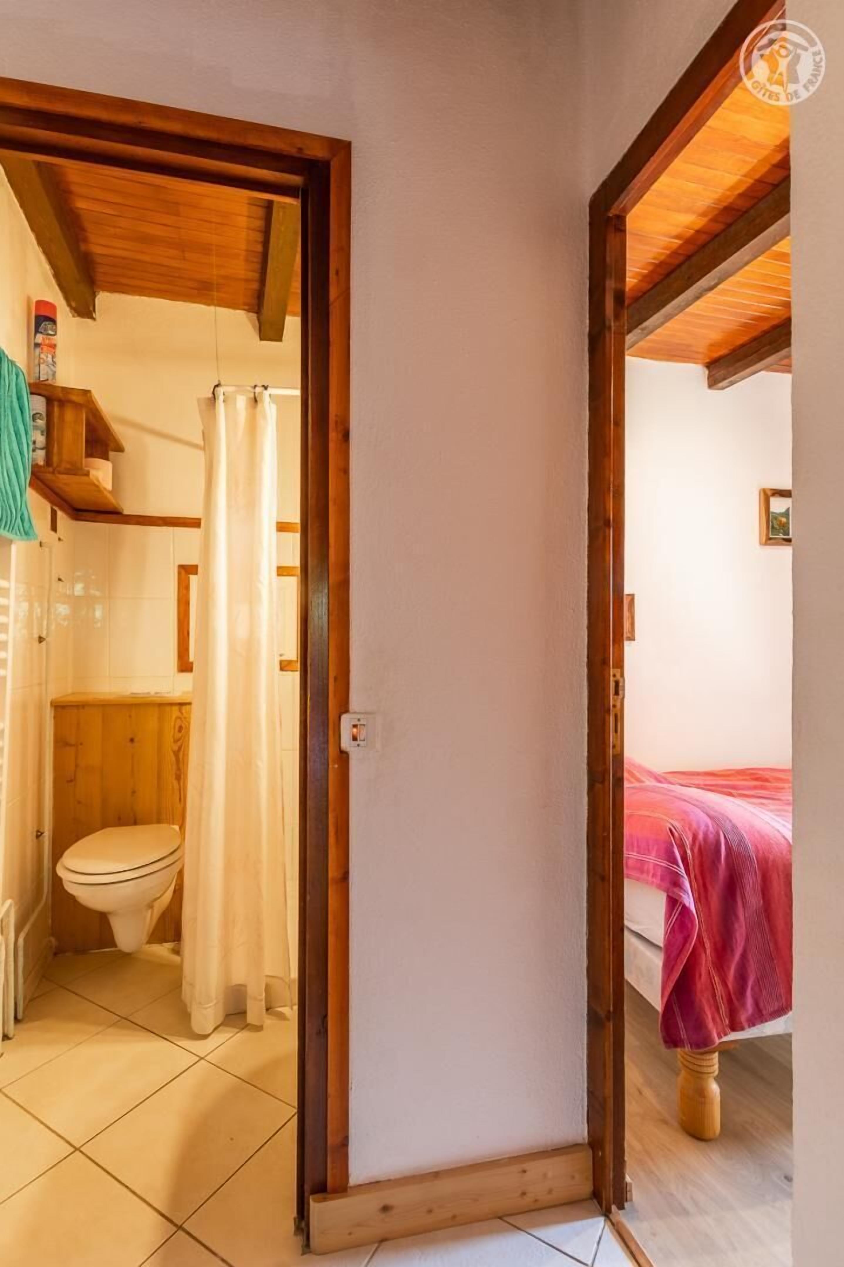 Ein schmaler Flur mit Holzboden und einer Tür zu einem Badezimmer mit Toilette und Duschvorhang.