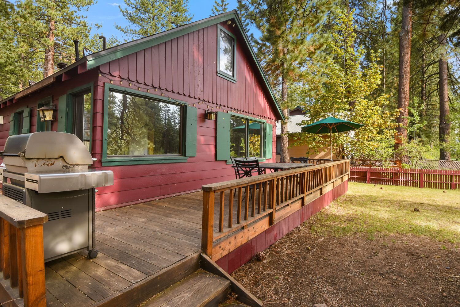 A cabin with a deck, outdoor grill, and a red fence.