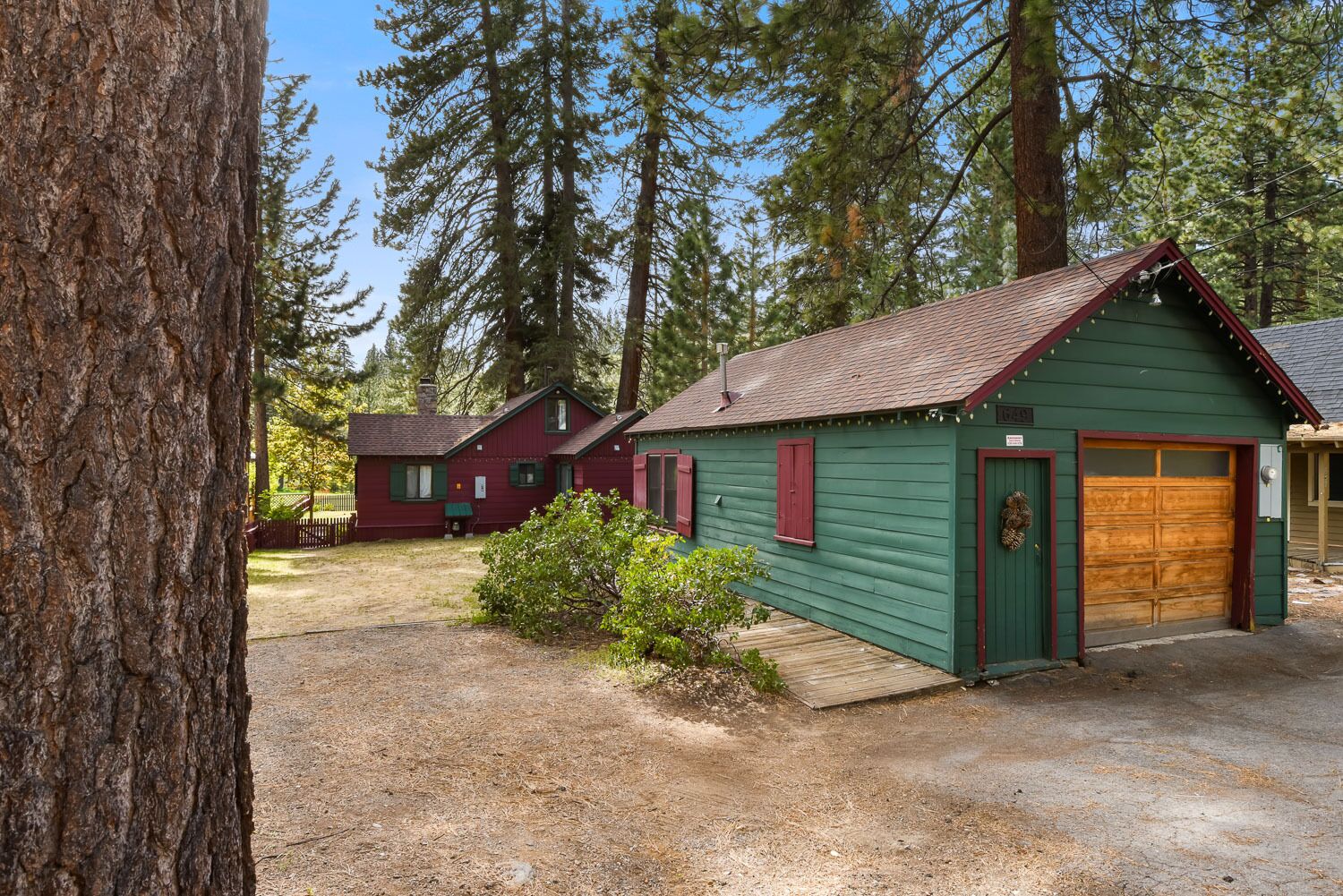 A cabin with a green exterior and a red roof, surrounded by tall trees.