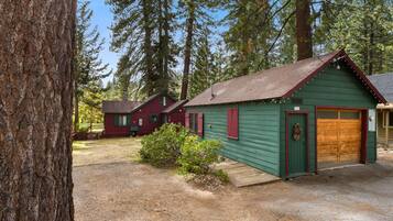 A cabin with a green exterior and a red roof, surrounded by tall trees.