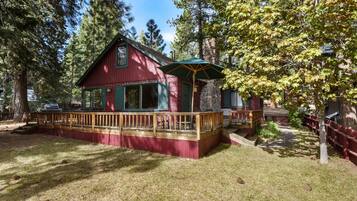 A cabin with a wooden deck, stone chimney, and a covered outdoor seating area.