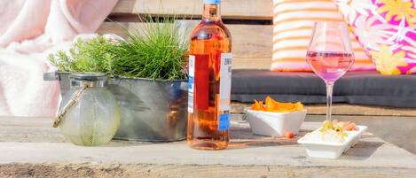 Una botella de vino Zinfandel, una copa de vino rosado, un colador metálico con plantas verdes y un cuenco blanco con comida sobre una mesa de madera.